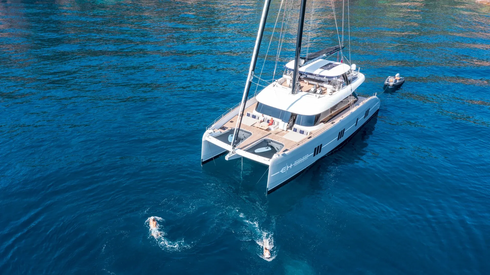High aerial of Endless Horizon II at anchor, foredeck lounge and tender astern