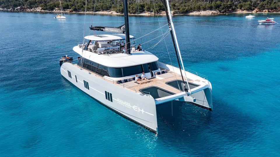 Aerial three-quarter view at anchor over turquoise water off a pine-covered shore