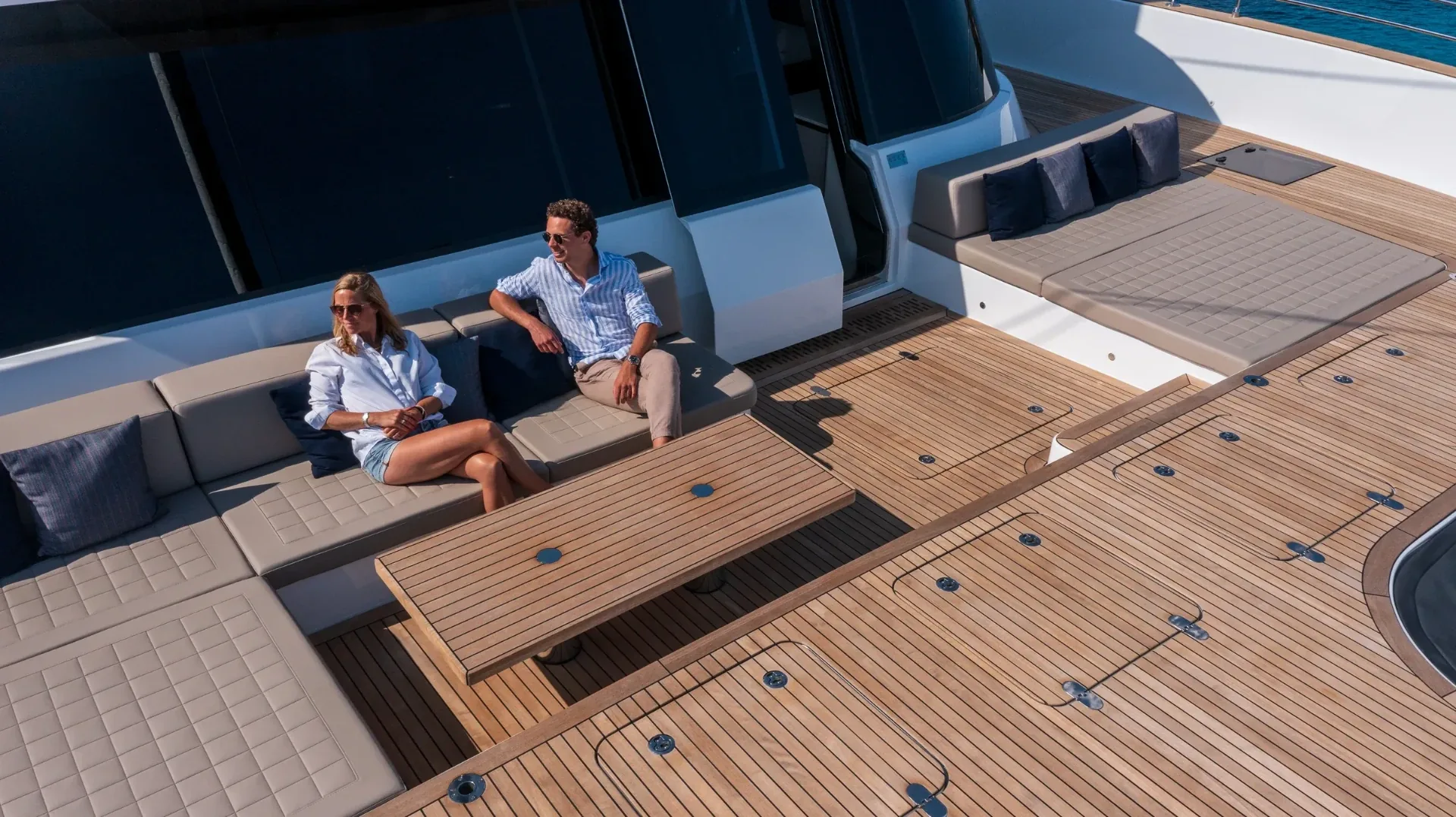 Two guests relaxing on the shaded foredeck lounge seen from above