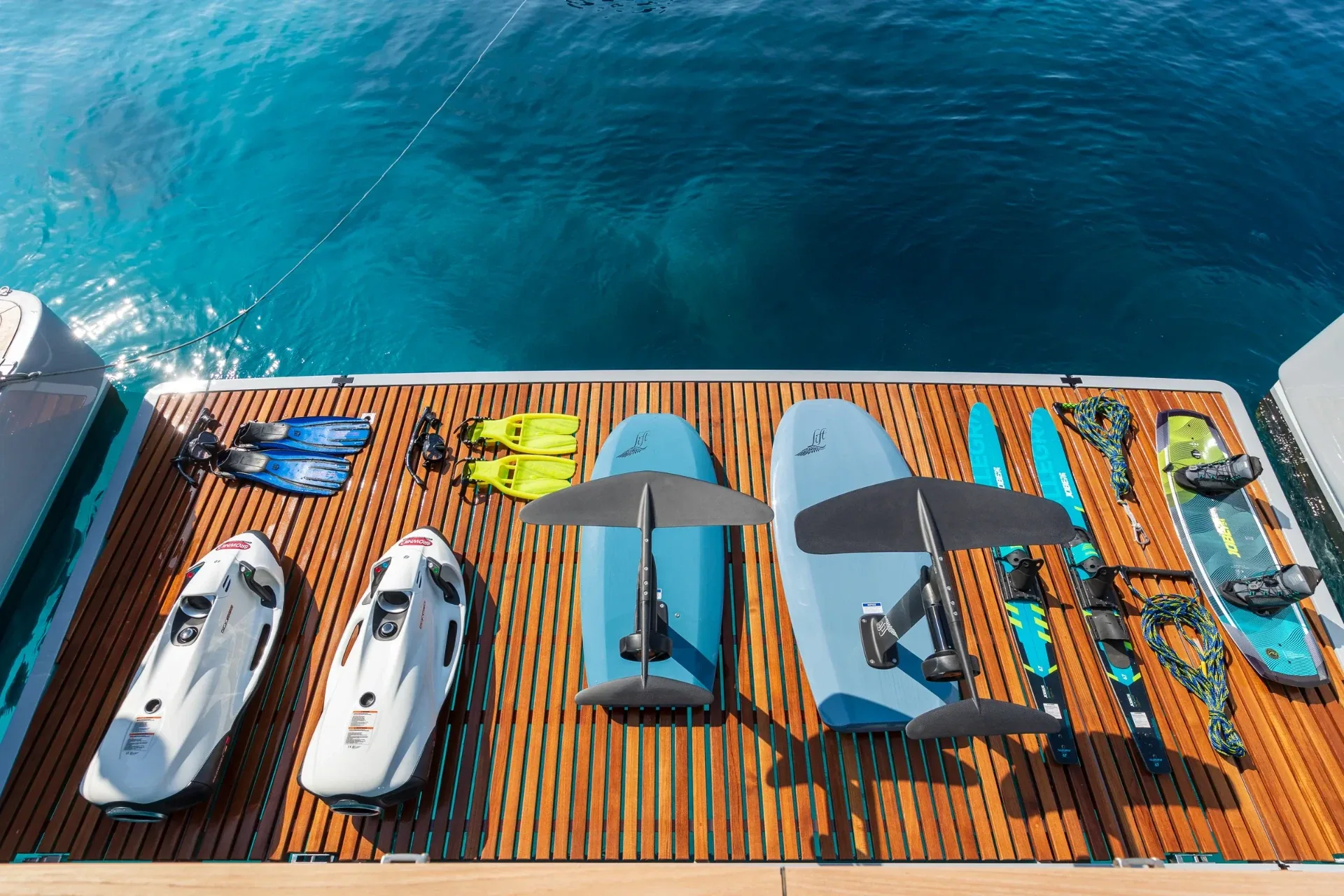 Seabobs, foil boards, skis and snorkel gear laid out on the teak swim platform