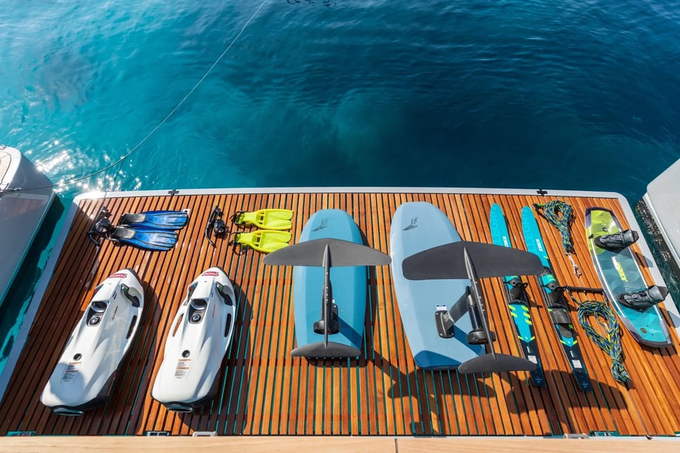 Seabobs, foil boards, skis and snorkel gear laid out on the teak swim platform