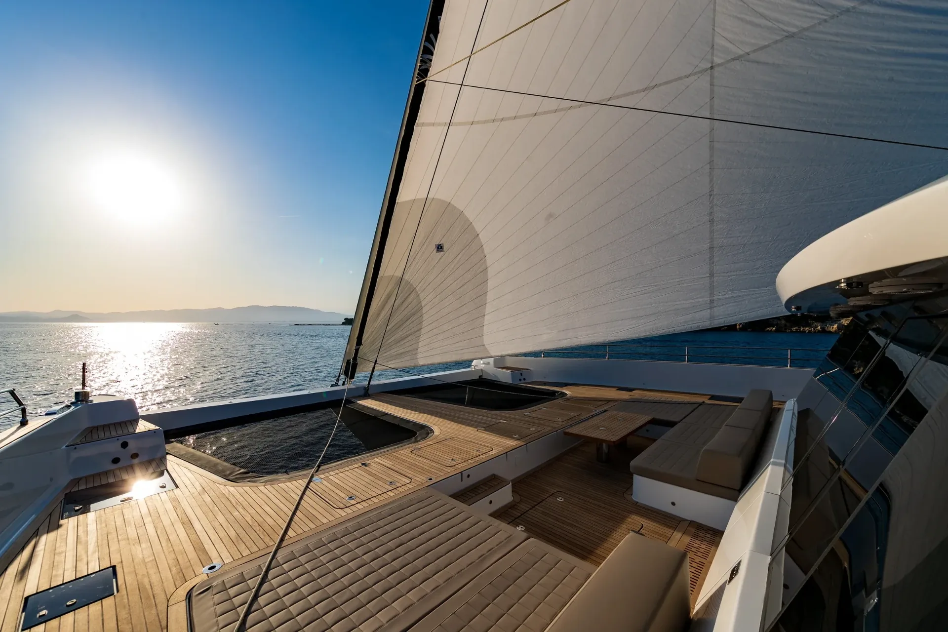 Teak foredeck and trampolines under sail with low sun across the water