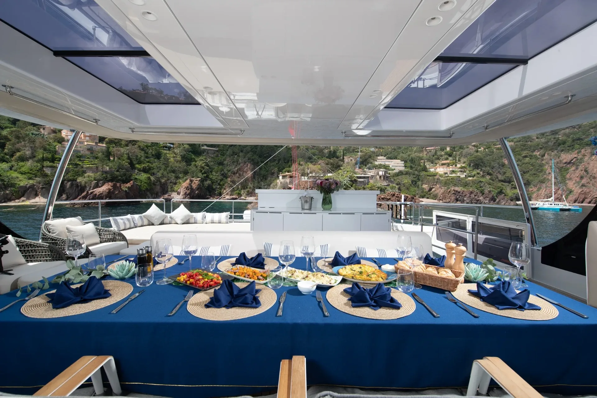 Cockpit table laid for lunch in blue linen, open to a red-rock cove astern