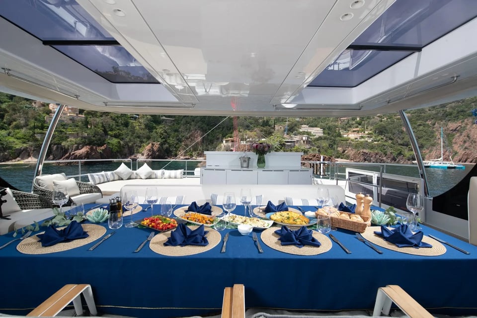 Cockpit table laid for lunch in blue linen, open to a red-rock cove astern