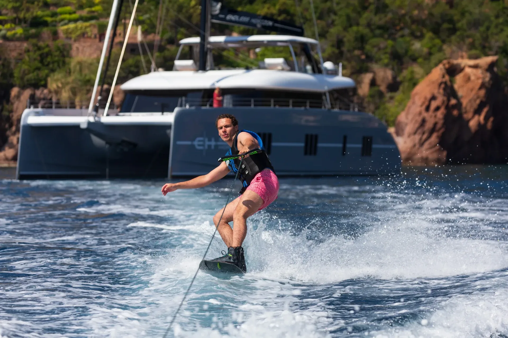 A guest wakeboarding past Endless Horizon II anchored below the red Esterel cliffs