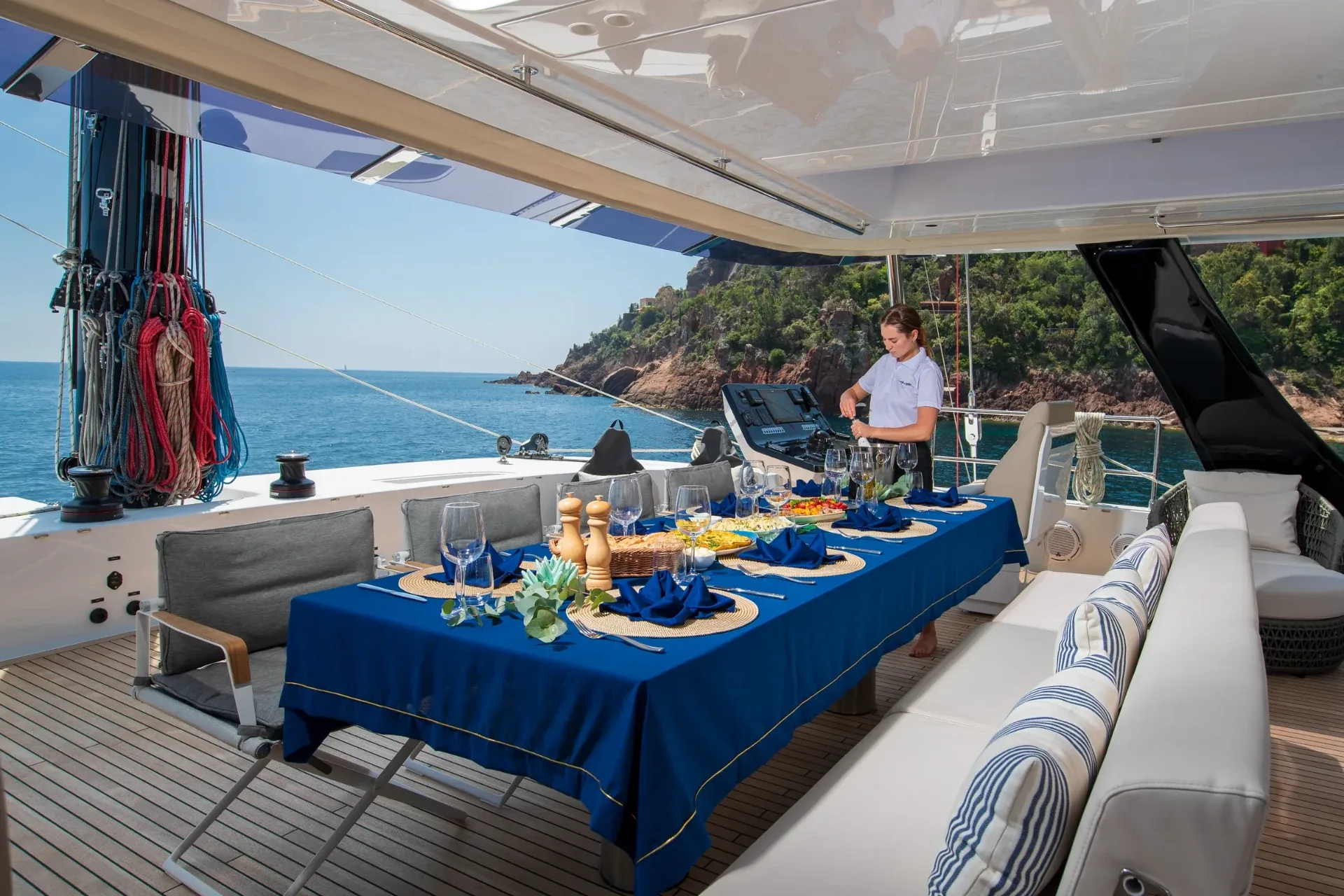 Stewardess pouring wine at the alfresco table with the coastline behind