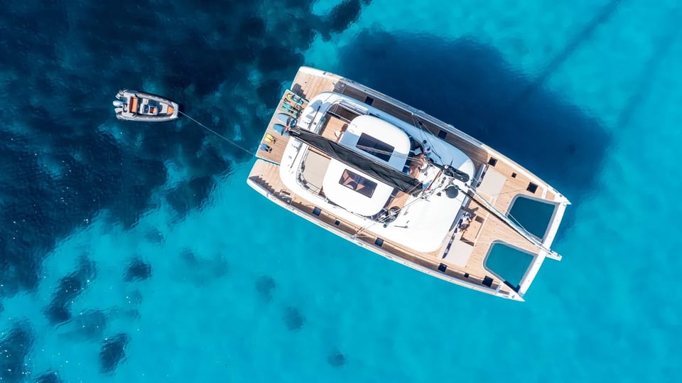 Top-down view over clear shallows with the tender streamed astern