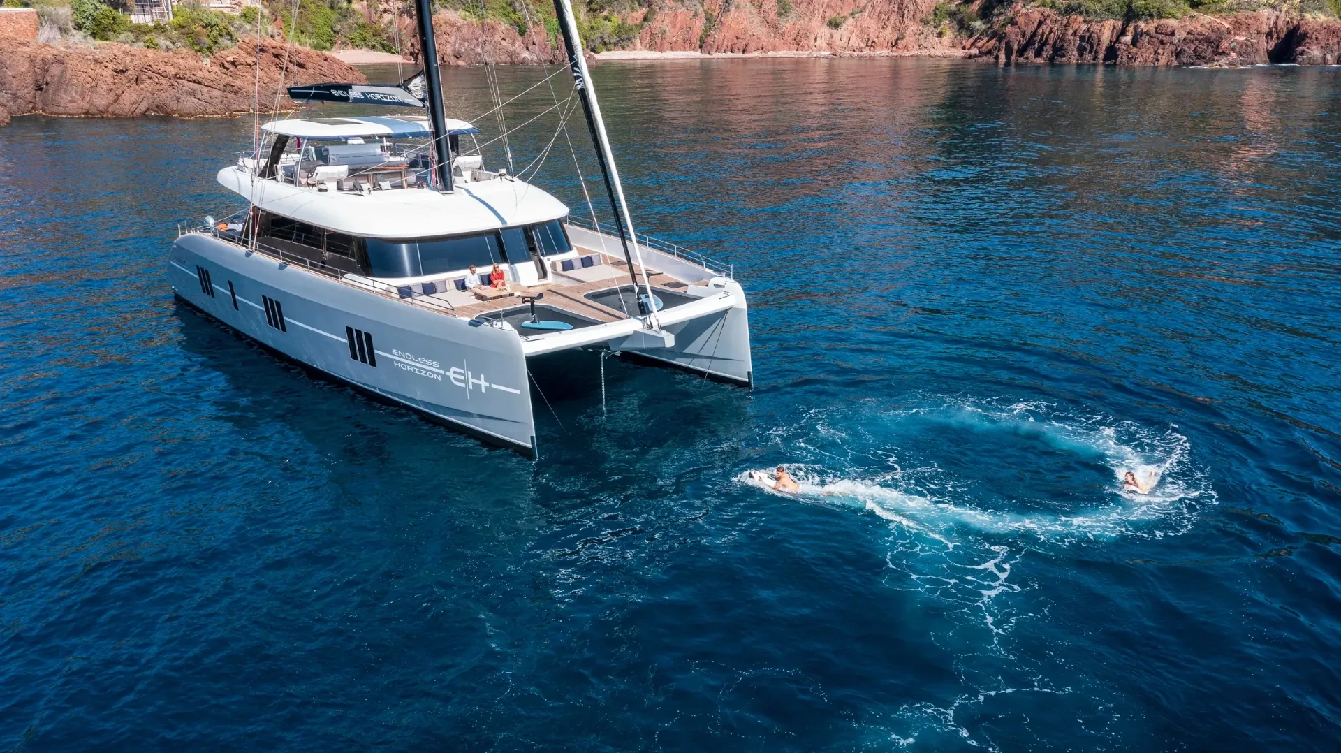 Endless Horizon at anchor below red Esterel cliffs with guests swimming astern
