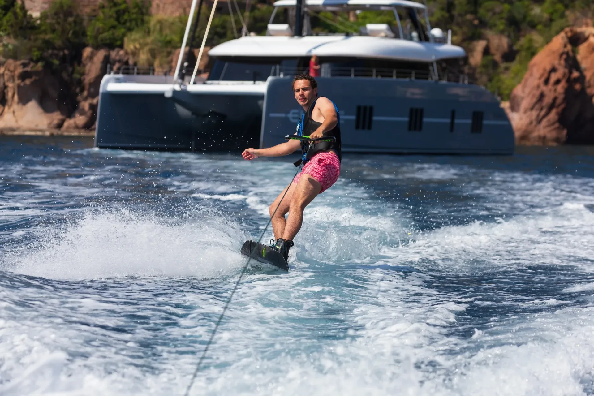 Wakeboarder carving through the wake with the catamaran at anchor behind