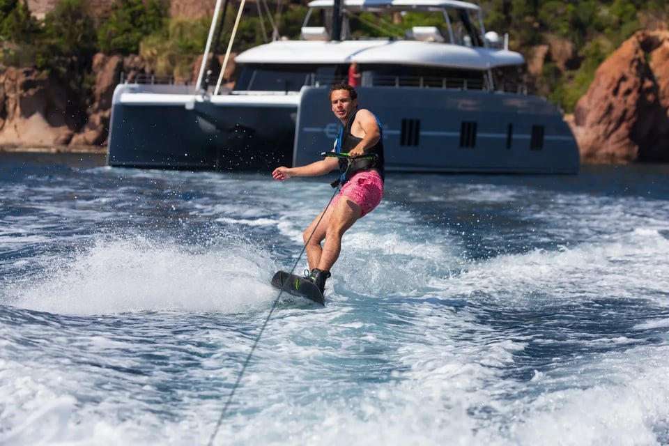 Wakeboarder carving through the wake with the catamaran at anchor behind